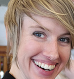 a white person around 30 years ol with short, straight blonde hair smiles into the camera